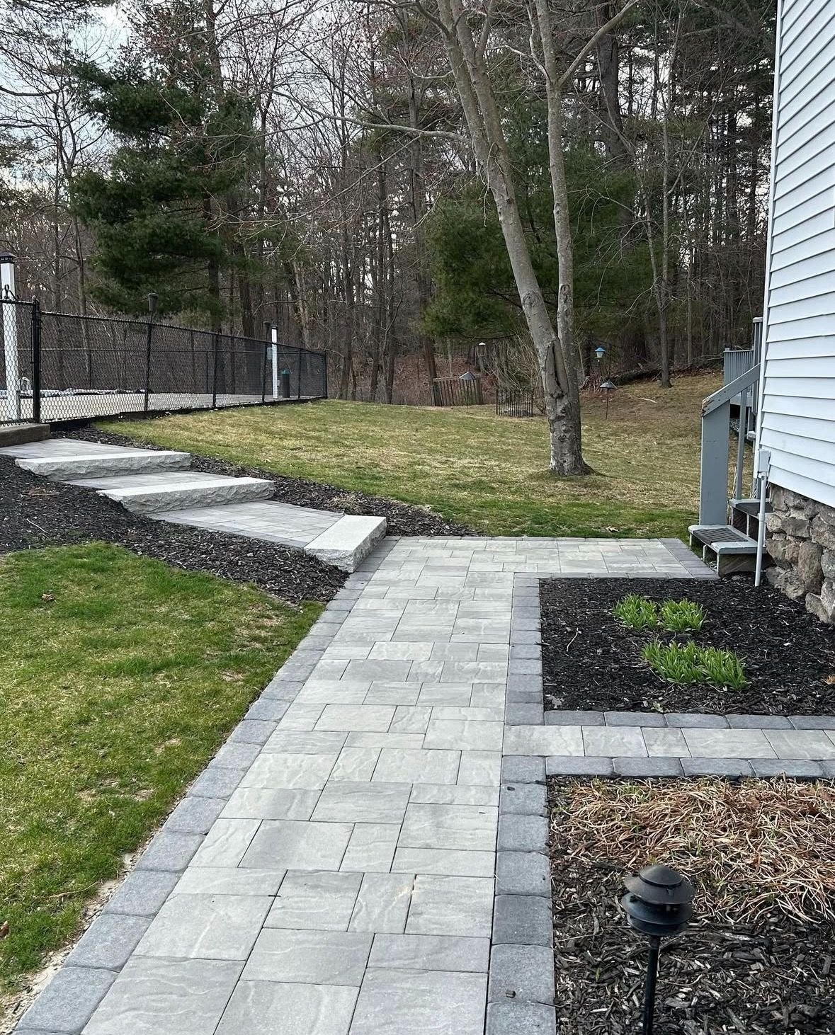 Finished paver walkway and bluestone steps leading to a fenced backyard