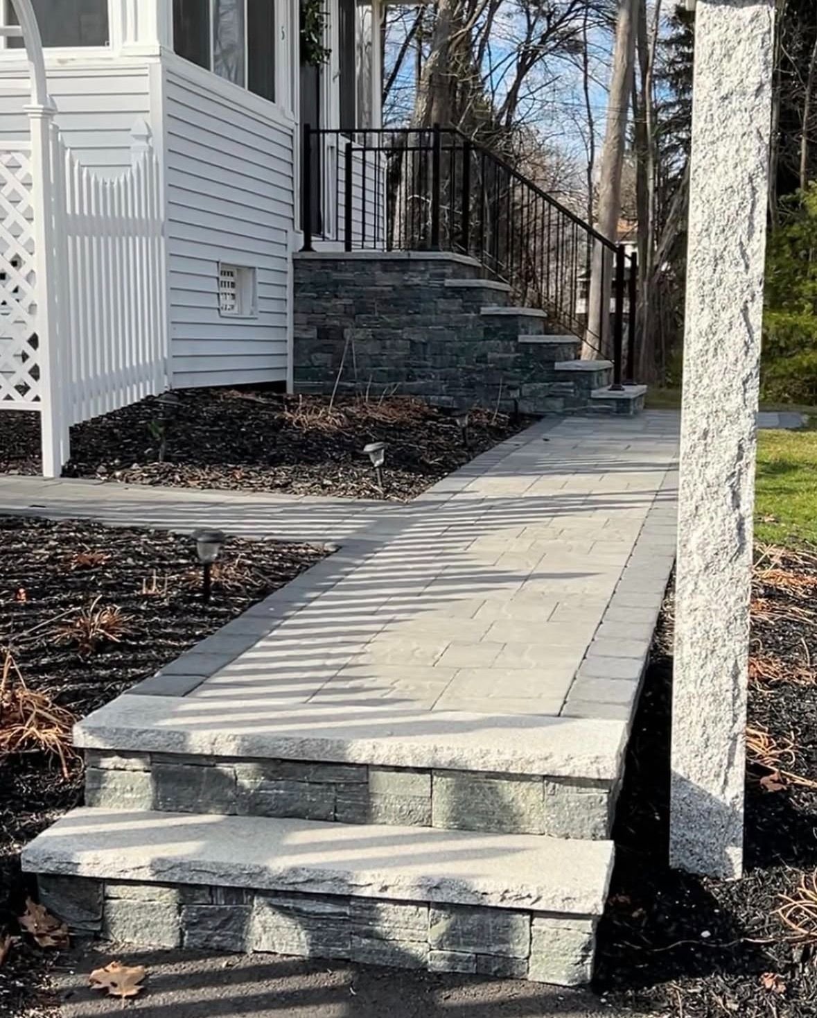 Finished stone-clad entry staircase with granite treads and a new paver walkway