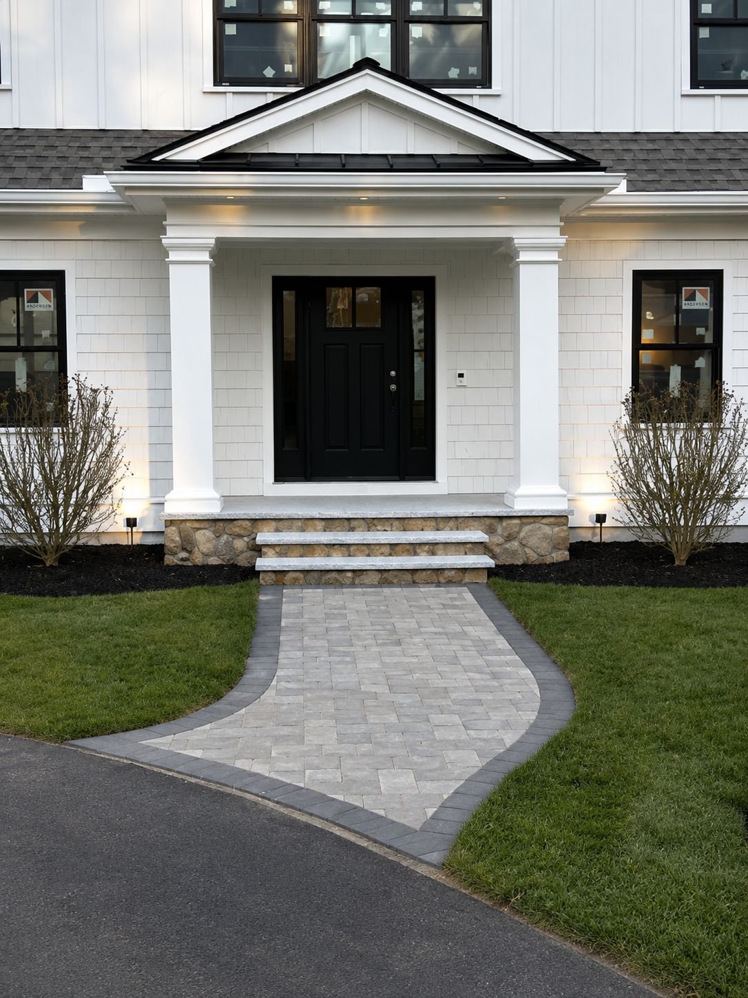 Finished Truestone entry with granite steps, fieldstone-clad porch, and a curved paver walkway