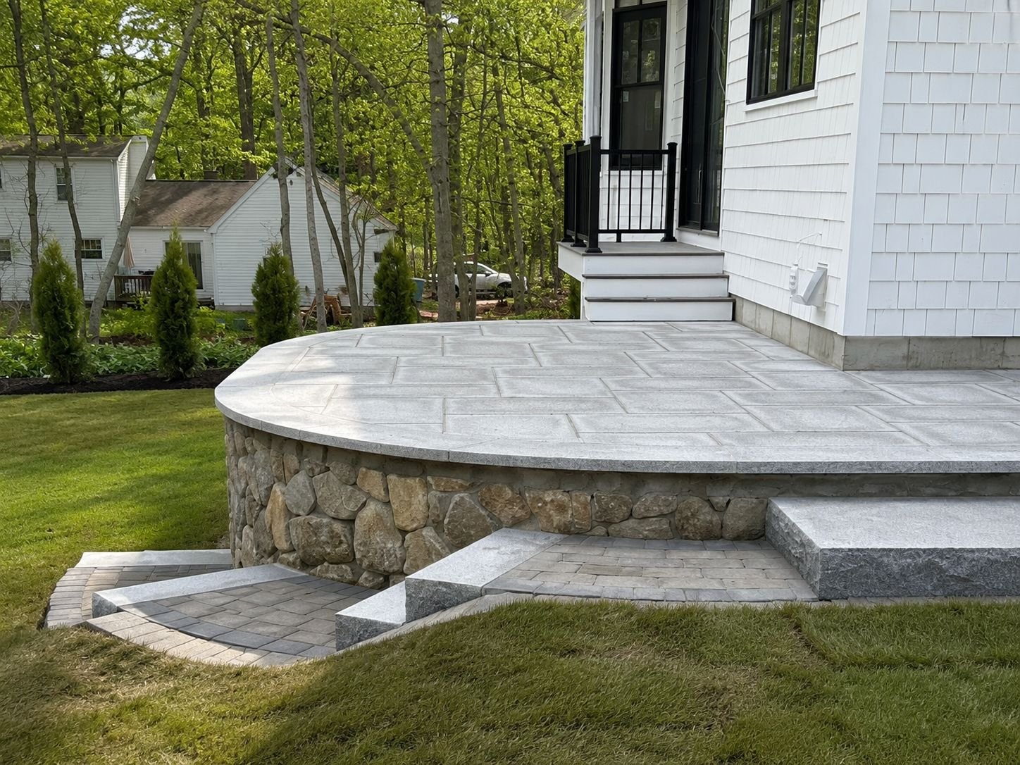 Coursed fieldstone veneer wall beneath a curved bluestone patio, a Truestone masonry project