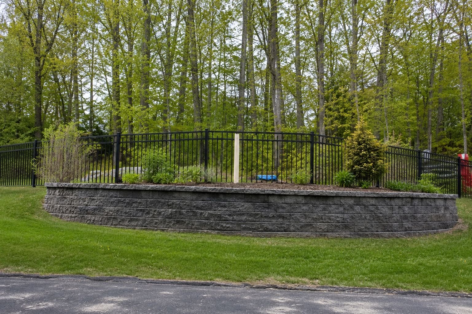 Curved segmental block retaining wall with a raised planting bed and aluminum fence, a Truestone retaining wall project
