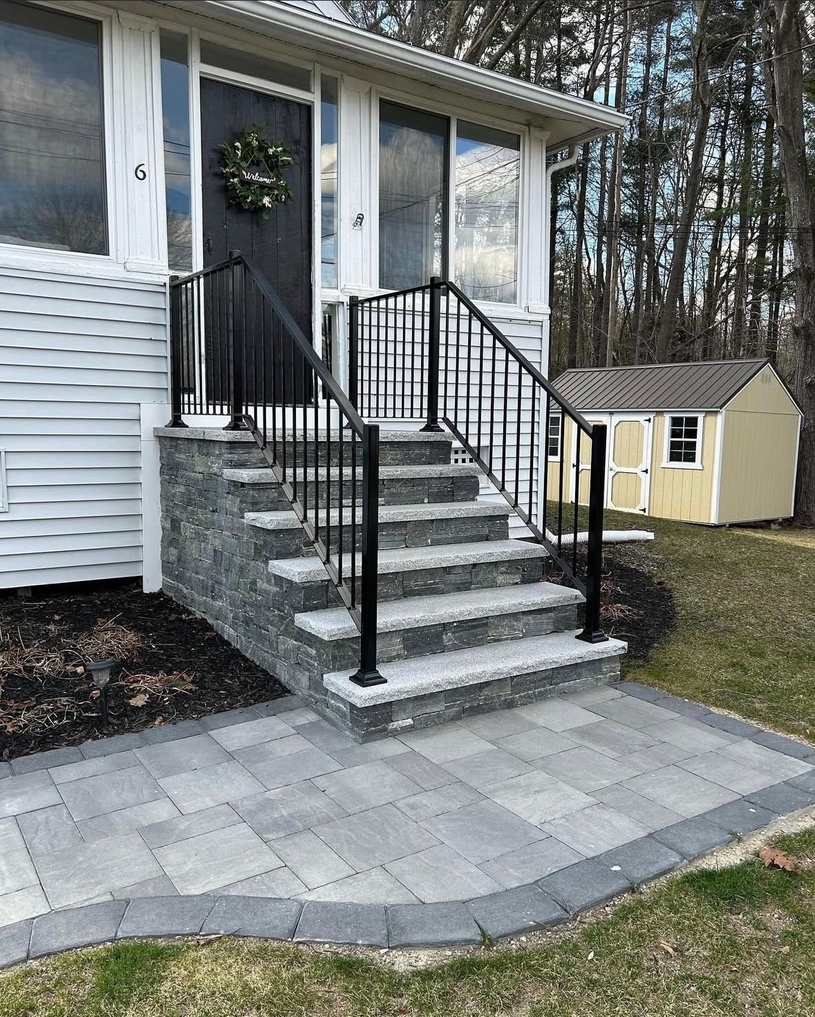 Finished coursed stone veneer staircase with granite treads and black metal railing