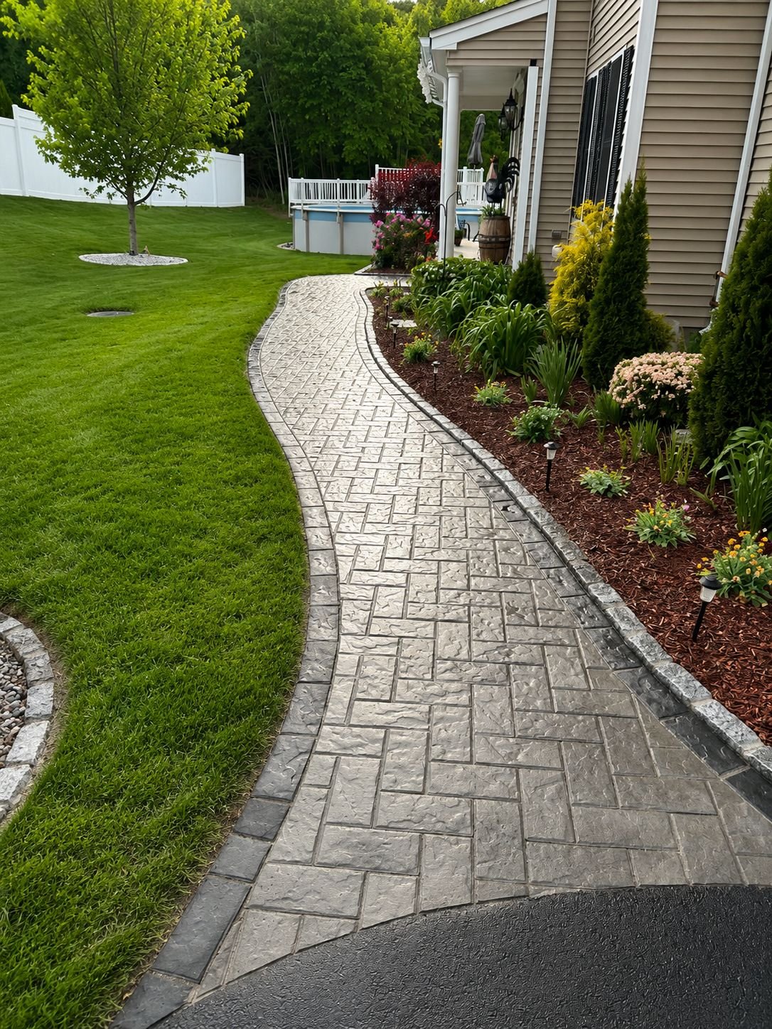 Herringbone-pattern paver walkway curving through a landscaped backyard, a Truestone patios and walkways project